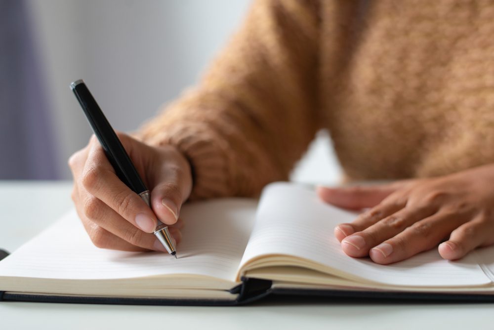 Close-up of businesswoman making notes in personal organizer. Unrecognizable lady writing in diary. Planning time concept