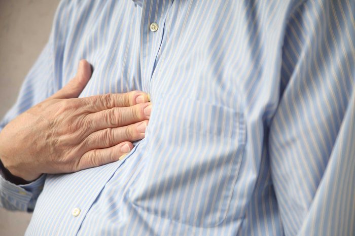 Man in a button-down blue dress shirt holding his right hand over his heart.
