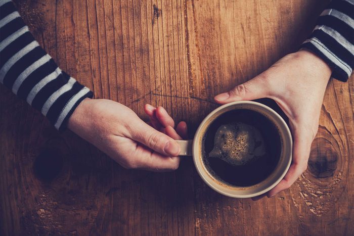 hands holding a mug of black coffee
