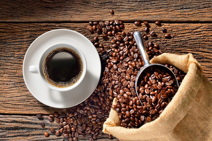 cup of coffee on saucer and bag full of coffee beans with scoop