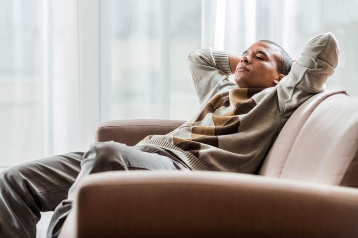 man relaxing on couch with eyes closed, hands behind head