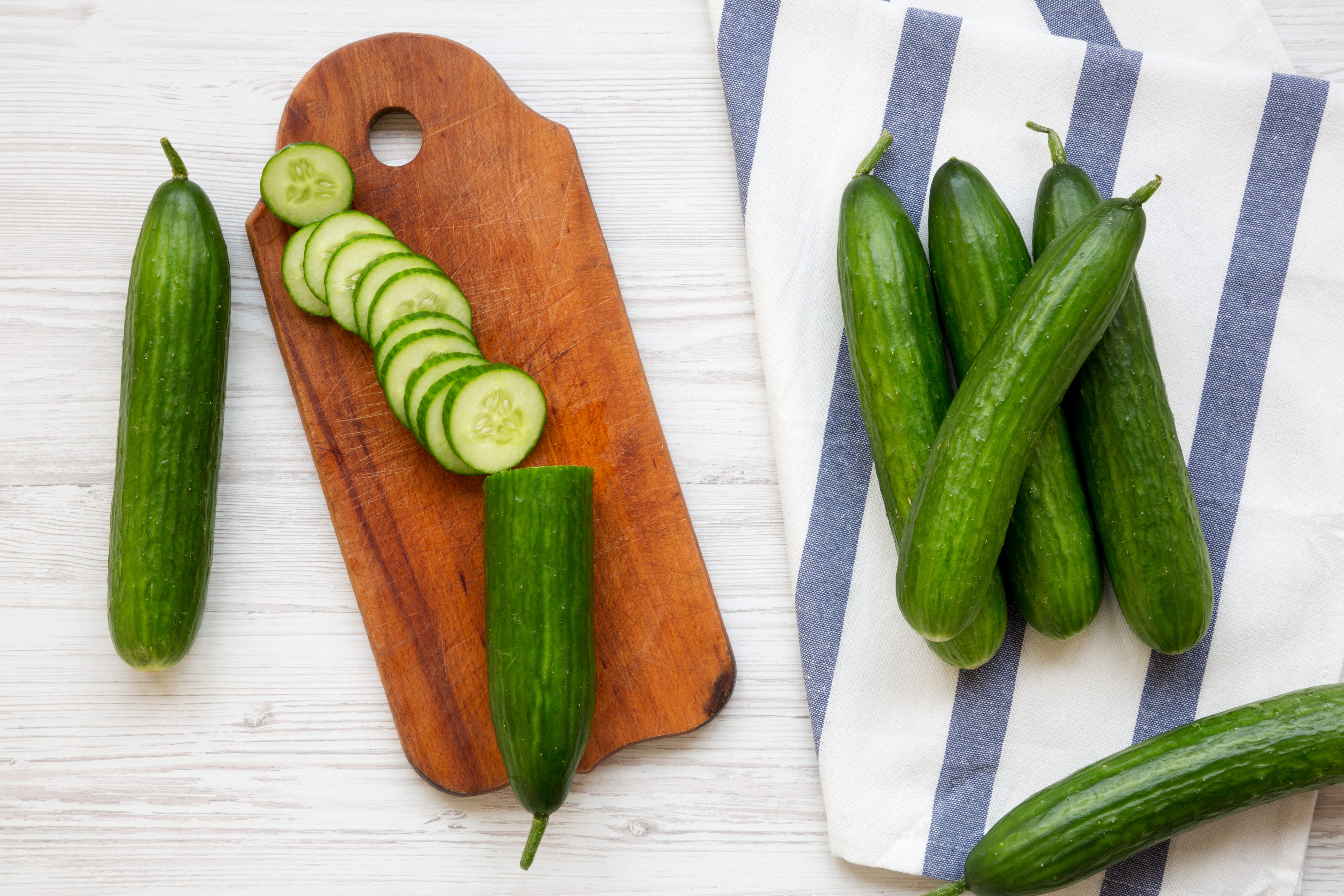Fresh raw green cucumbers, top view. Flat lay, from above, overhead. White wooden background.