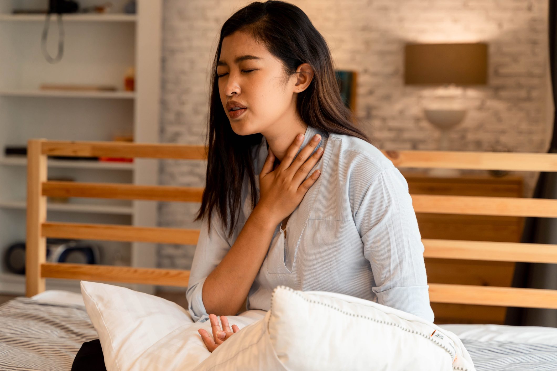 Portrait of 20s young Asian woman suffering pain and medical sickness in bedroom at night. Sore Throat, neck related pain symptoms