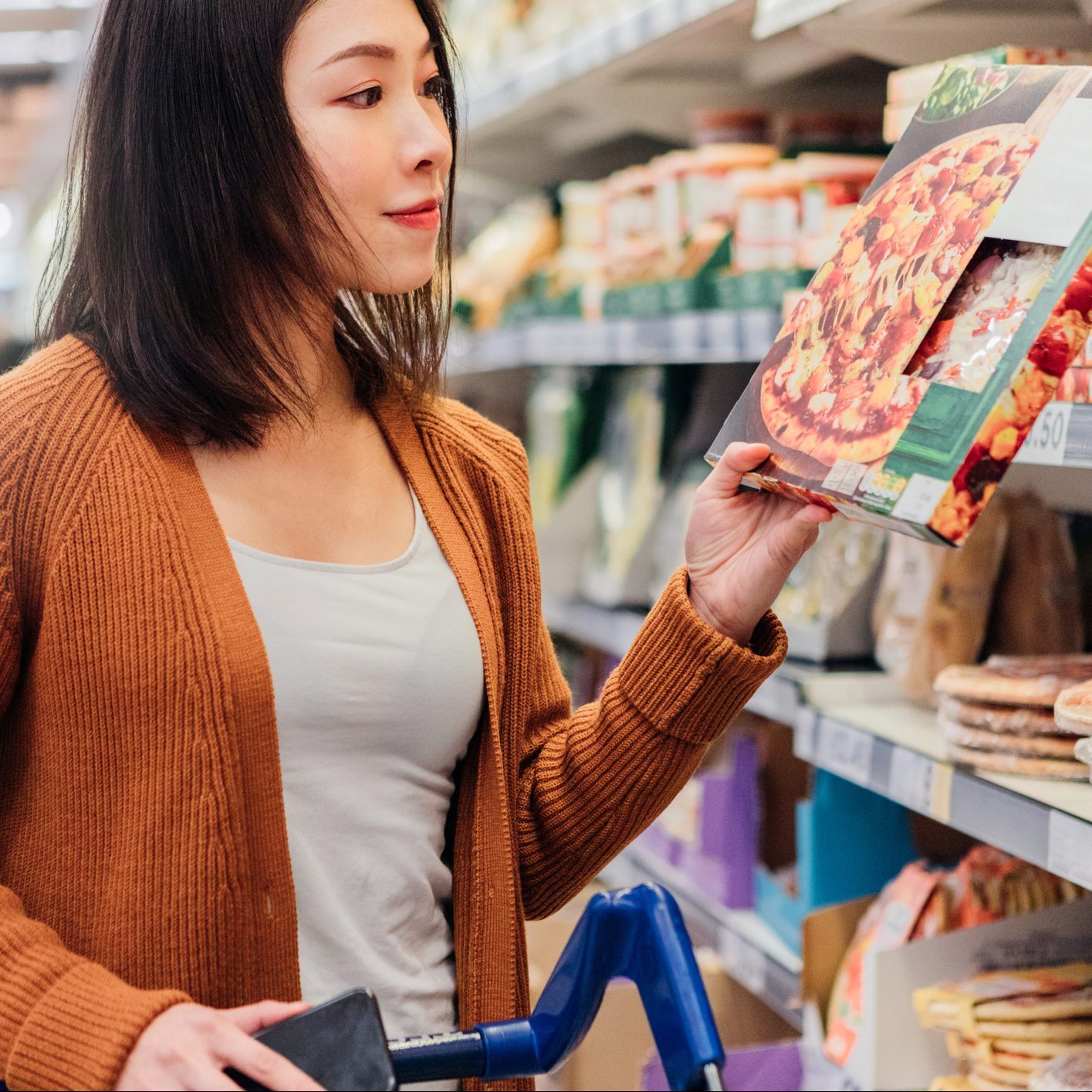 Young Asian woman picking up a packaged pizza in grocery store